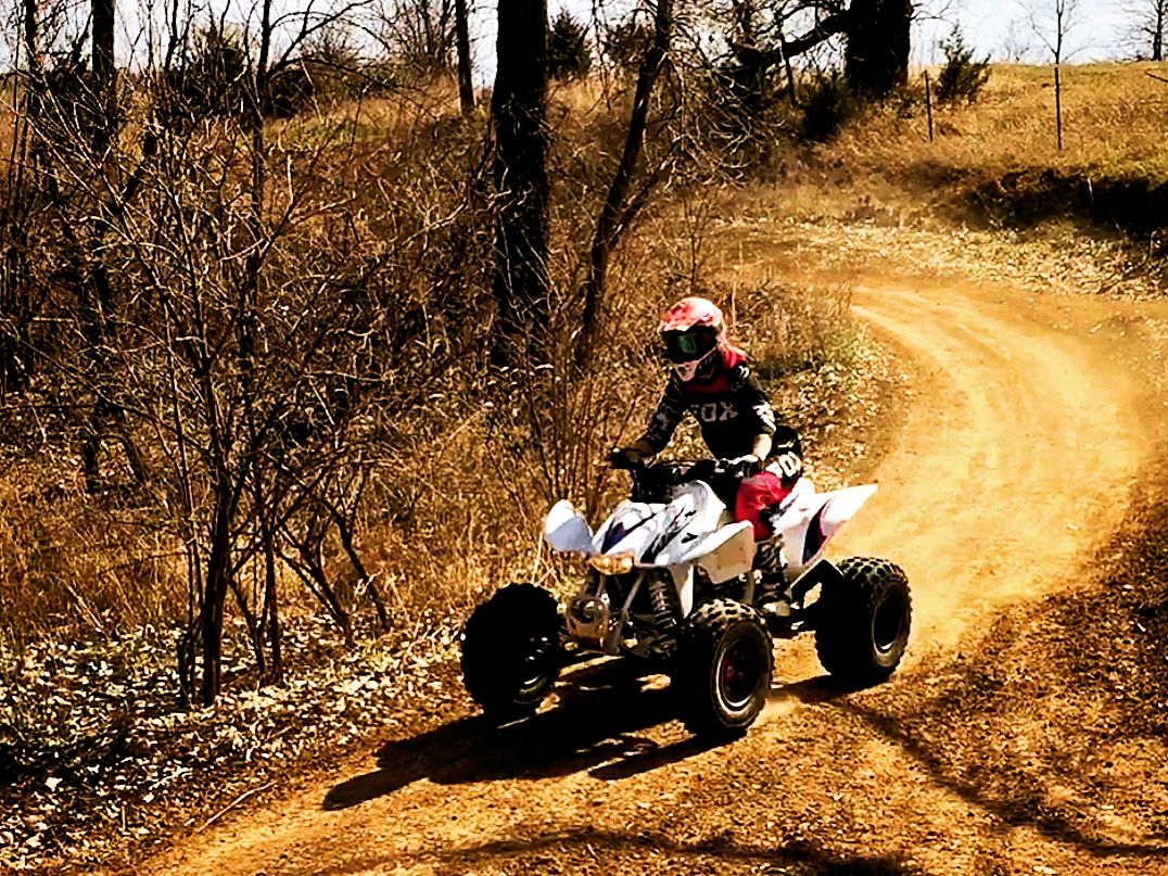 Young woman riding ATV around beginner motocross track.