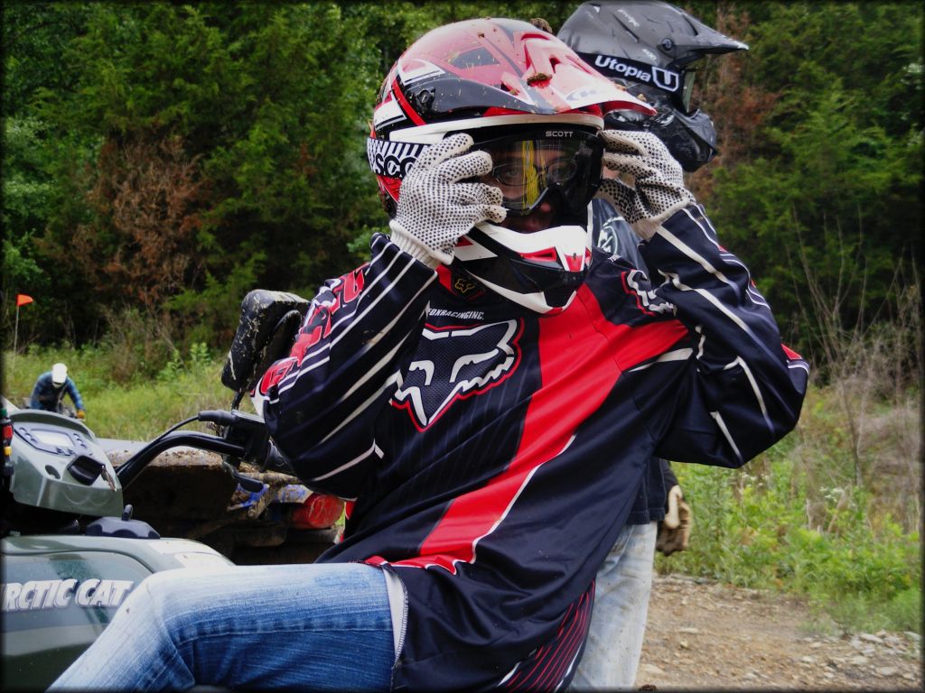 Young rider wearing red and black motorcycle helmet, Scott goggles and Fox Racing motocross jersey sitting on Artic Cat ATV.