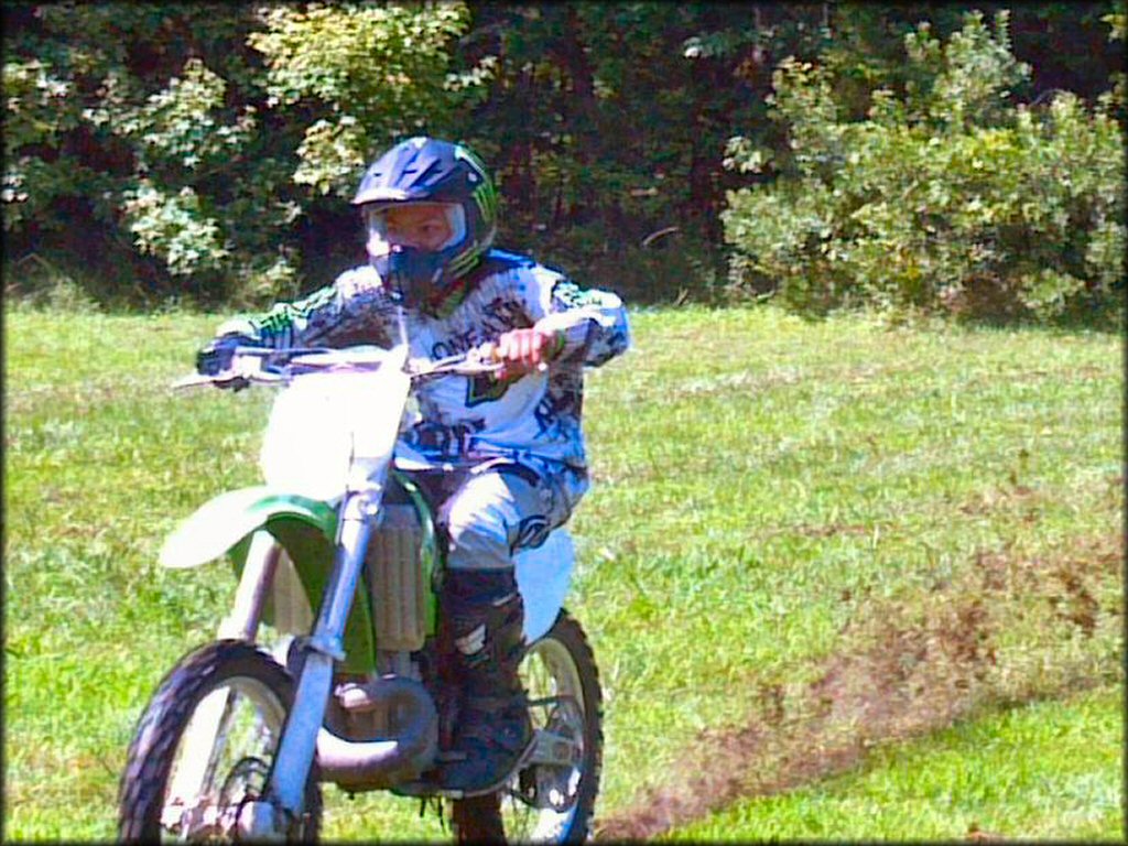 Young man wearing O'Neal motocross gear on KX two-stroke going through grassy field.