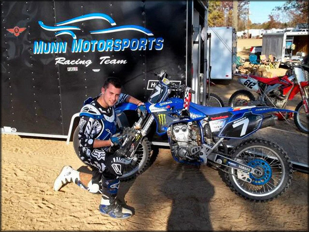 Rider with Fox Racing motocross gear and Alpinestar boots kneeling next to Yamaha YZ450F.