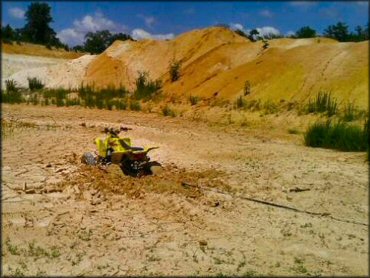 A Yellow ATV attached to a tow strap to be pulled out of deep mud puddle.