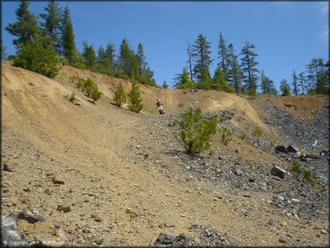 Suzuki RM250 two-stroke going down trail in gravel pit.