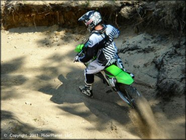 Young man wearing Shift black and white motocross gear riding Kawasaki four-stroke through deep sandy berm.
