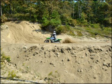 KX dirt bike going up sandy hill on motocross track.