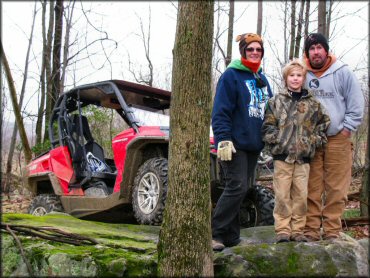 A Young Family Standing on a Rock in front of their Can-Am UTV on a Wooded Trail