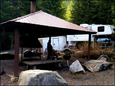 Large gazebo with concrete pad and picnic tables surrounded by large rock boulders.