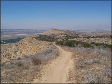 A close up photo of a narrow motorcycle trail along the ridgeline of steep mountain.