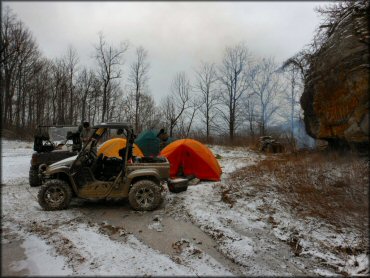 Three UTVs parked at primtive campsite with three tents and camping gear.