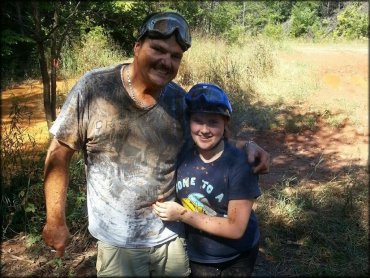 Man and woman standing next to each other covered in mud and wearing goggles.