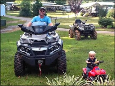 Man sitting on ATV next to toddler sitting on Power Wheels Quad.