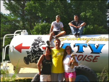 Group photo of young adults standing and sitting next to Sunnyside ATV park water tank.