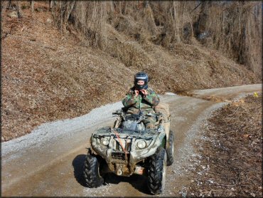 ATV with winch, camouflage plastic and mud tires on gravel road.