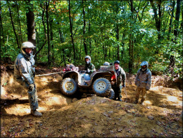 Four people using a tow rope and winch to pull ATV from deep rut.