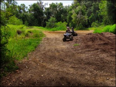 Two kids riding quads on trail.