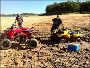 Honda ATV with a winch on the back bumper trying to pull out antother ATV stuck in the mud.