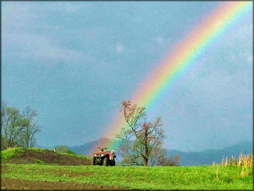 Red four wheeler parked in grassy meadow with rainbow in background.