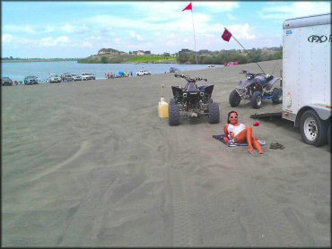 Two ATVs with orange whip flags parked next to box trailer with young woman nearby.