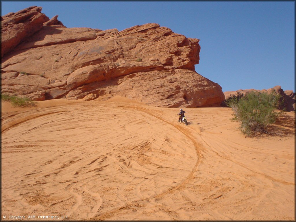 Man on Suzuki RM-250 riding up small sandy hill.