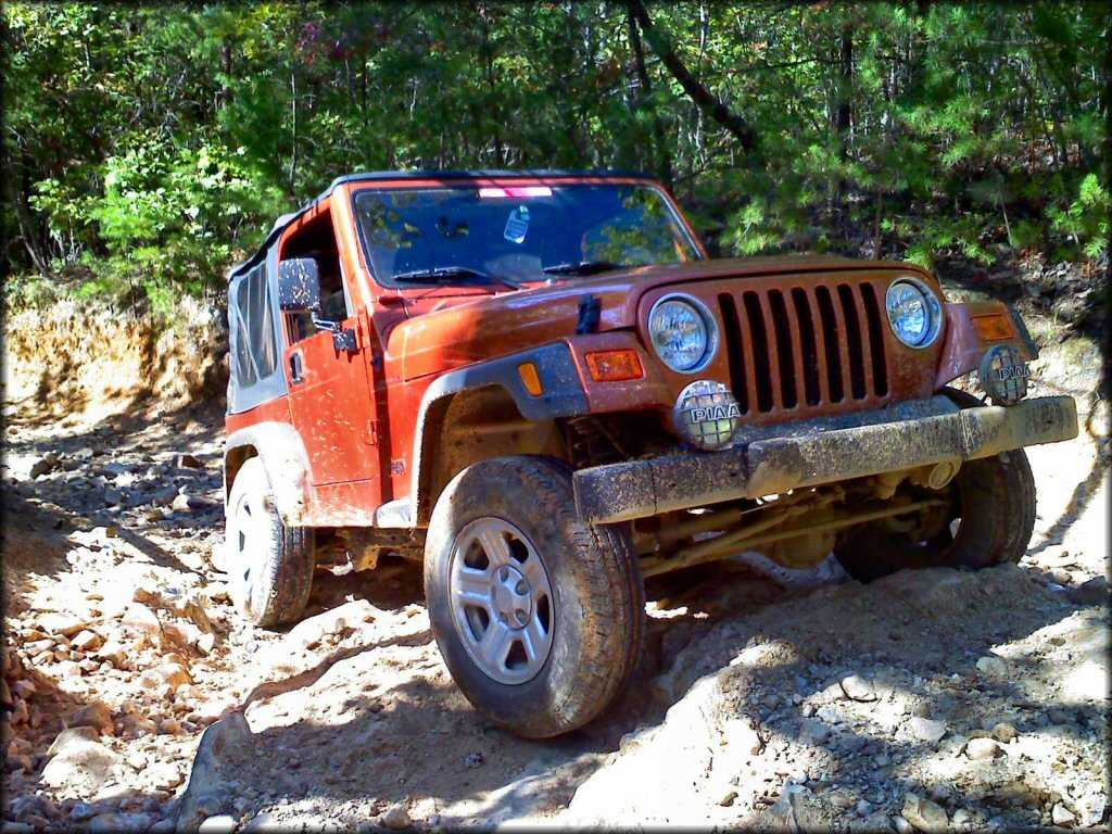 4x4 Jeep with alloy rims and PIAA lights climbing a rocky section of trail.