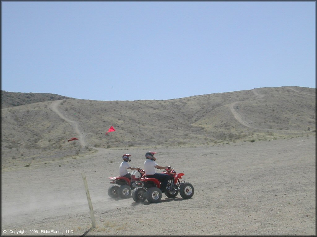 Two Honda ATVs each with red whip flags and one carrying a cooler strapped to the rear.
