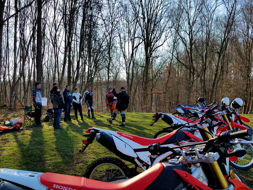 A group of students listening to a coach at a dirt bike school with a fleet of Honda dirt bikes in the foreground