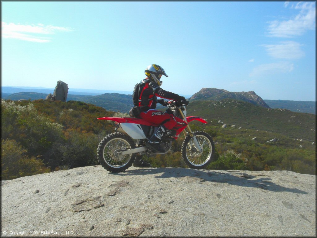 Man on Honda CRF250 parked on lage rock with scenic view in background,