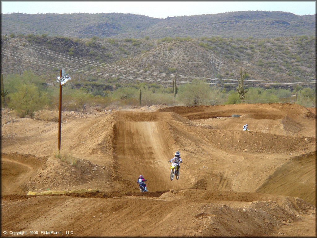 Young child on Suzuki mini dirt bike catching some air on a motocross track.