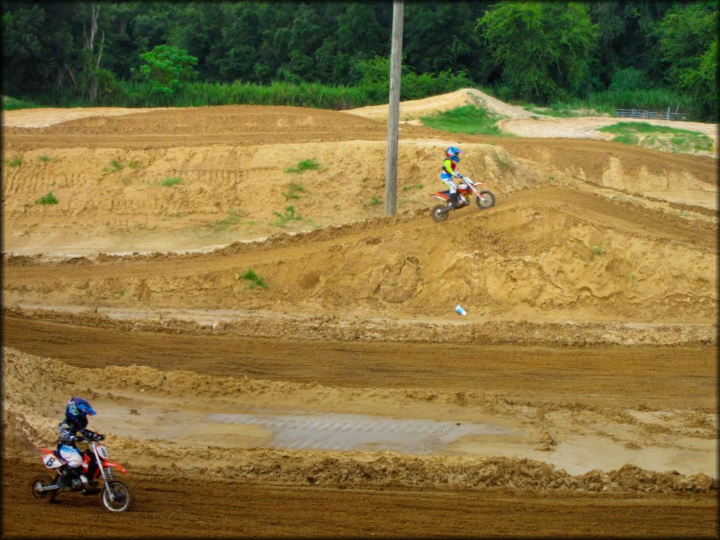 Two young kids on Honda 50cc dirt bikes riding on motocross track.