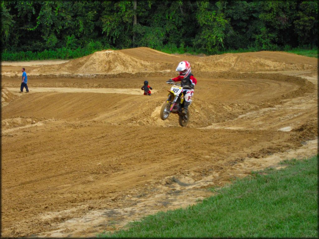 Young child on 50cc Suzuki dirt bike catching a little air from a small jump on motocross track.