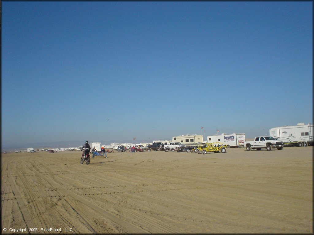 Man on dirt bike riding near primitive camp with RVs, trucks and dune buggies at Oceano Dunes.