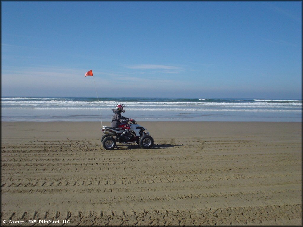 Young man on ATV with rear paddle tires and orange whip flag riding down the beach at Oceano Dunes.
