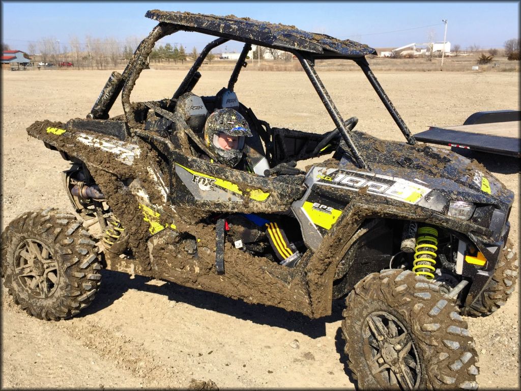 UTV covered in mud with young child wearing a motorcycle helmet in the passengers seat.