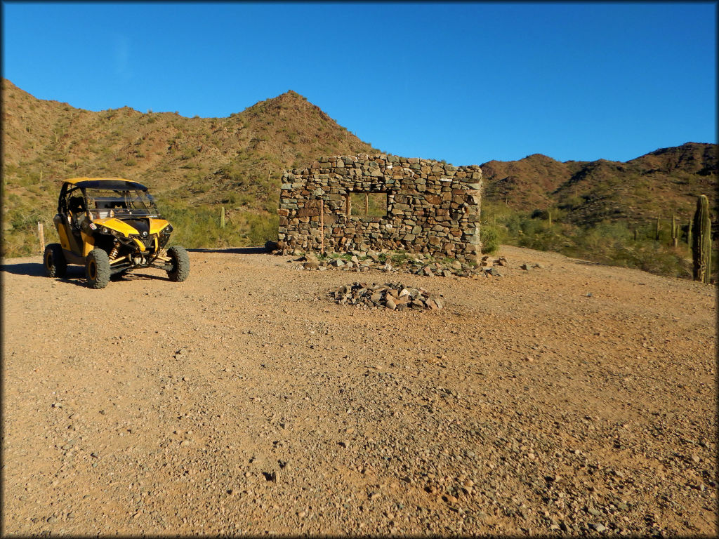 Yellow CanAm UTV parked next to stone cabin ruins.