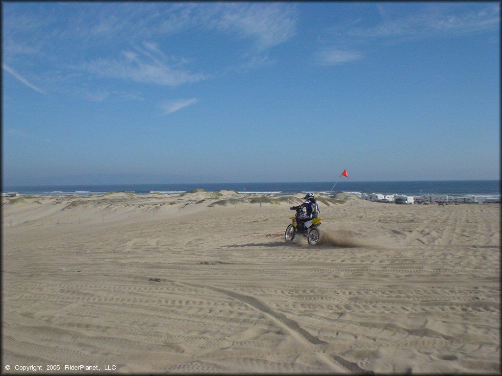 Young woman on Suzuki RM100 dirt bike with orange whip flag riding at Oceano Dunes.