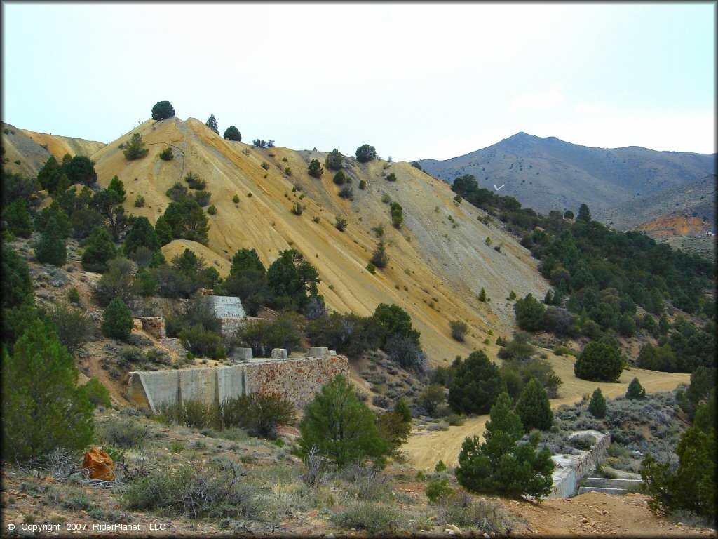 A scenic view of old mine ruins and steep hills with juniper trees.
