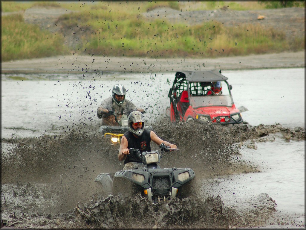 Two ATV riders and a UTV driver going through a deep mud hole at Atkinson Motorsports Park.