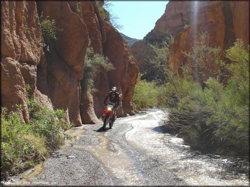 Man on Honda CRF-250 riding through gravel wash and shallow stream at the Box Canyon near Florence, Arizona.