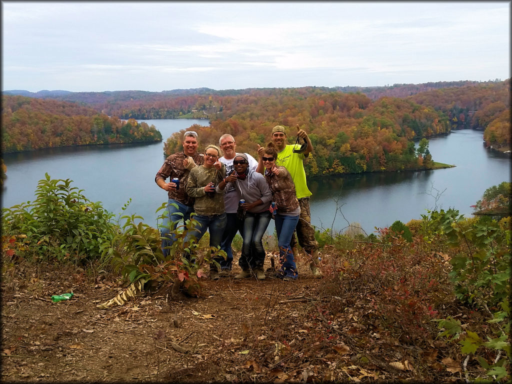 A group of friends posing with scenic river and trees in the background.