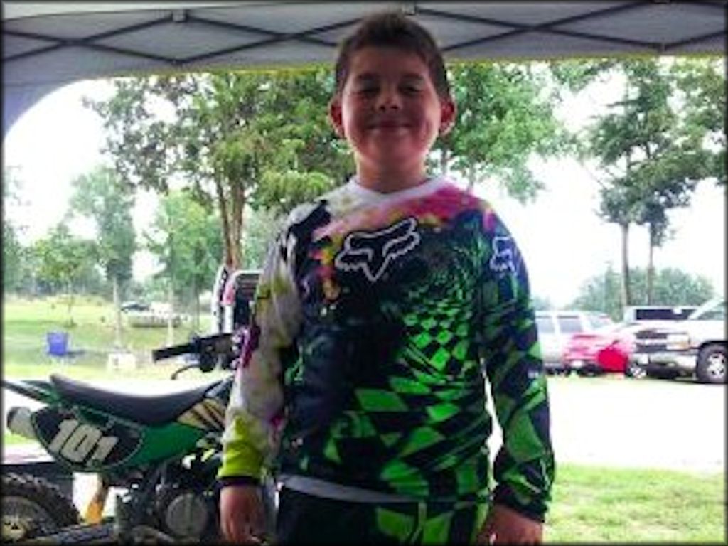 Young boy wearing Fox Racing motocross gear and green Kawasaki mini bike.