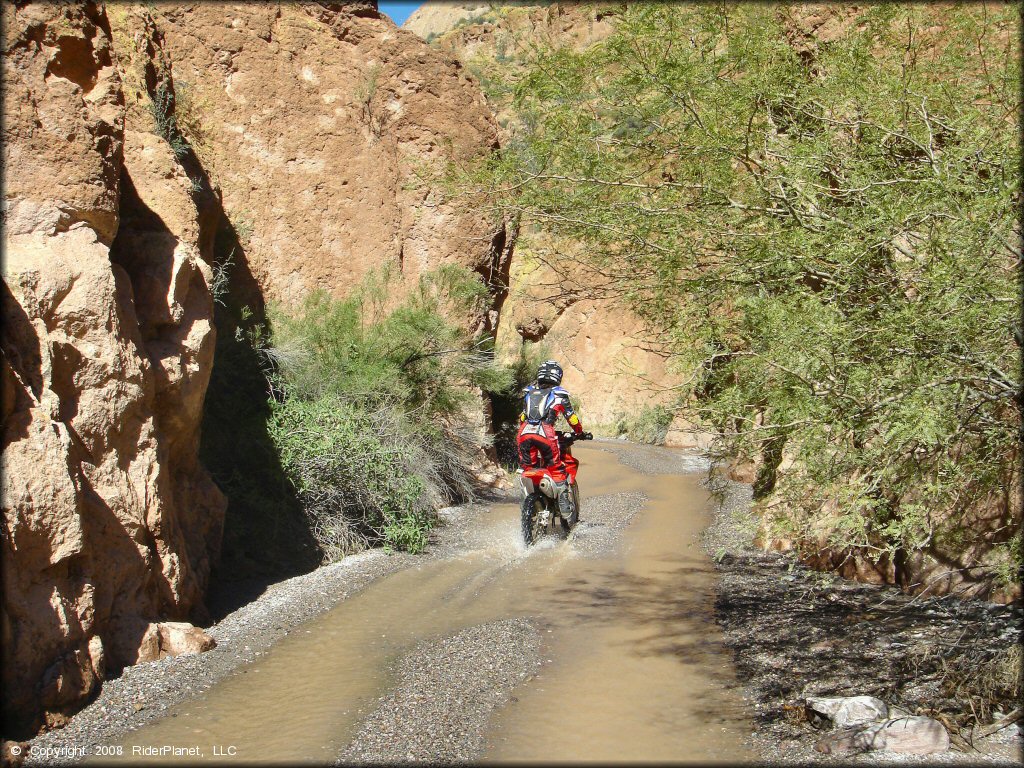 Honda CRF150R going through shallow stream in box canyon.