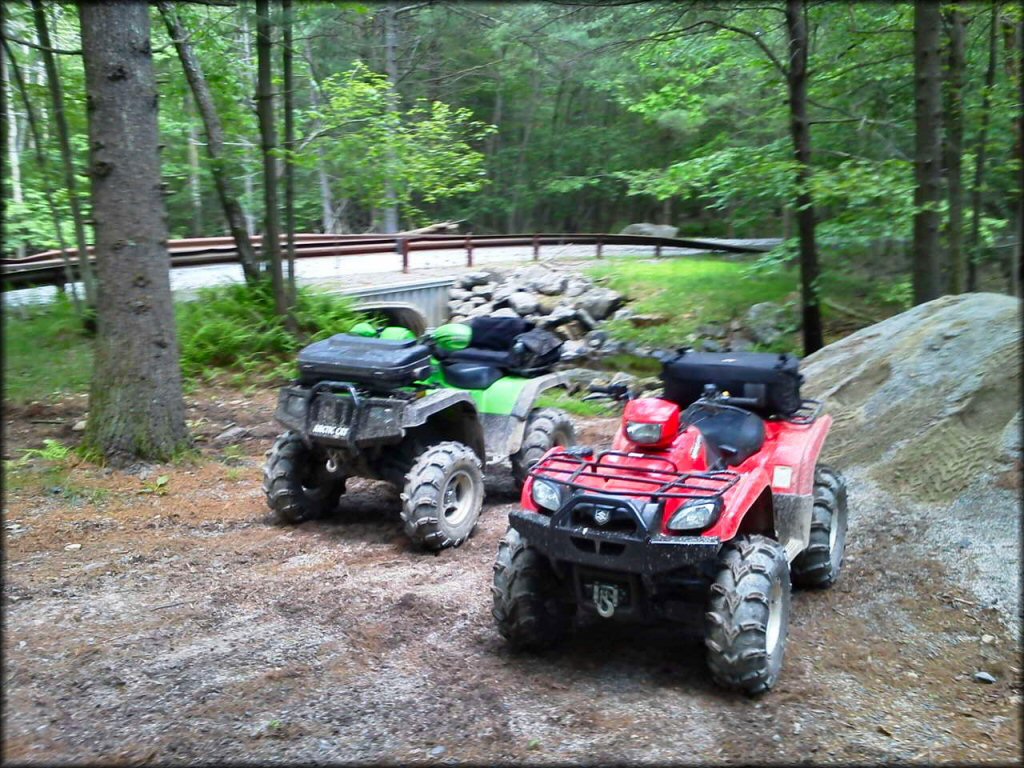 A green Arctic Cat ATV parked next to red Polaris Sportsman with winch attached to the front bumper.