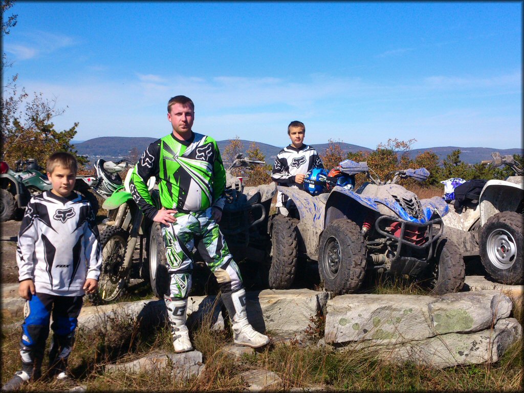 Man and two young boys standing next to four Yamaha ATVs and one Kawasaki dirt bike.