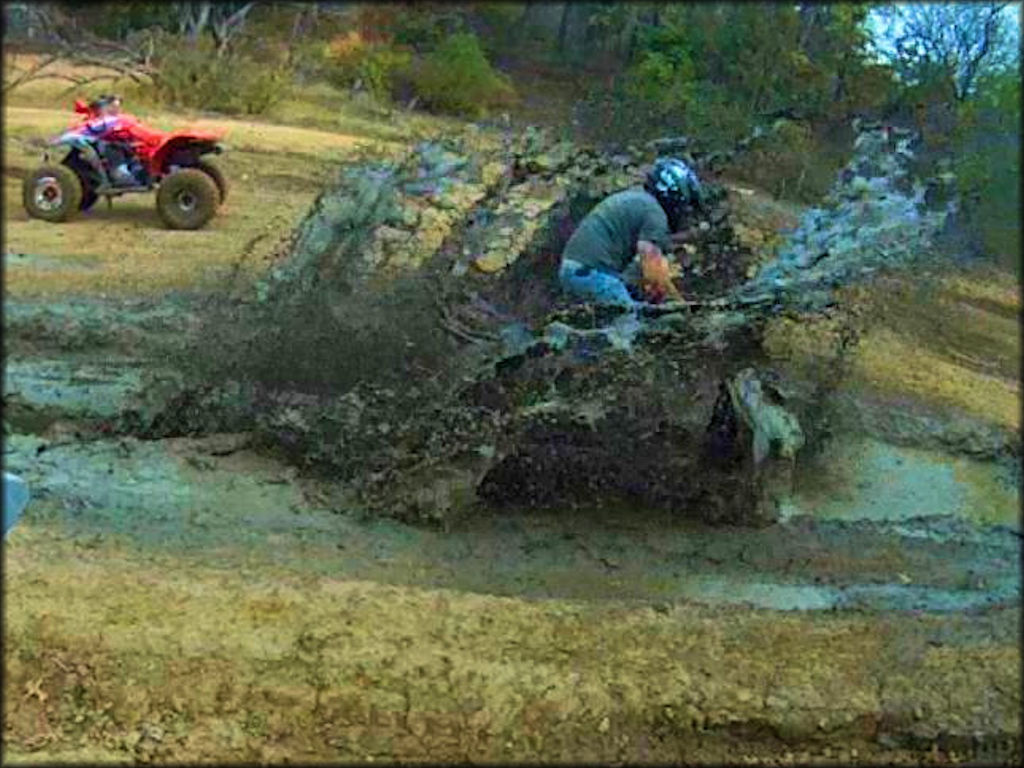 Man on ATV going through deep mud puddle.