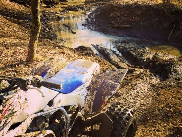 ATV covered in dirt parked nex to mud puddle.