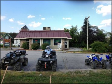 Two Arctic Cat ATVs and two Yamaha Raptors parked in front of restaurant parking lot.