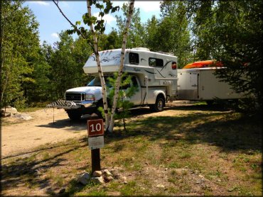 Ford truck with Bigfoot Camper attached to long trailer parked in campsite.