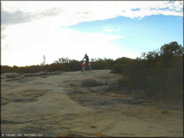 Man riding Honda CRF250X on solid rock ledge.