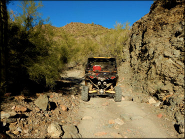 A dual exhaust Can-Am ATV on a desert trail with high rock walls.
