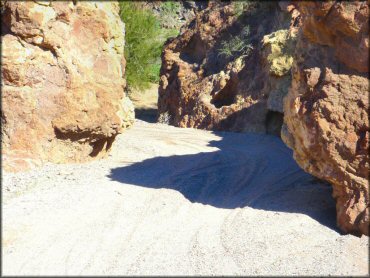 A close up photo of a sandy 4x4 trail that cuts through a narrow channel surrounded by rugged rock boulders.