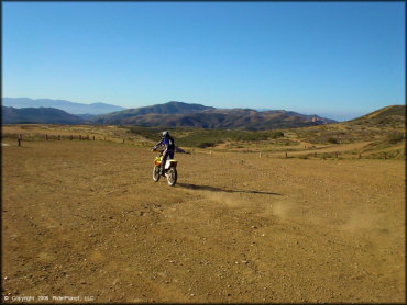 Young woman on Suzuki RM-250 dirt bike riding riding around staging area.